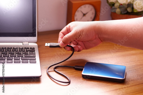 Man's hand was connecting an external portable hard disk usb 3.0 cable to laptop computer on desk, Data transfer or backup personal files concept photo