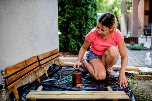 Young woman painting wooden fence in backyard, © Ana