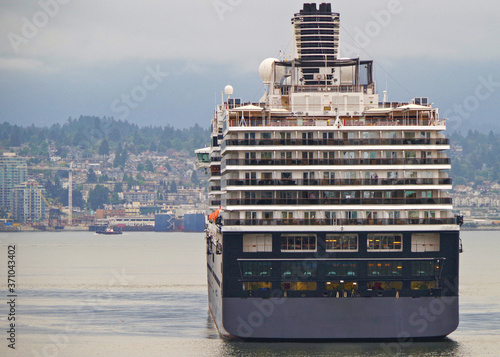 Stern of HAL or Holland America cruiseship or cruise ship liner against skyline of Vancouver, Canada with cargo or freighter vessel and mountains in background photo