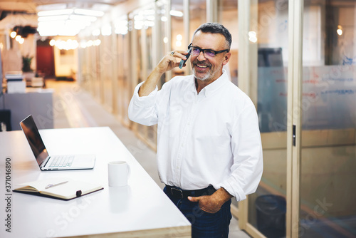 Cheerful businessman happy about accomplished successful project communicating via cellular.Matured owner of corporation getting good news from partners talking on smartphone on working break
