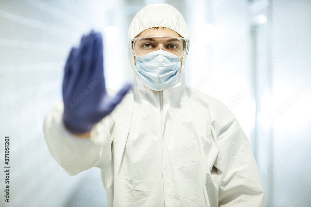 Corona virus concept. Male scientist doctor in mask, glasses and protective suit showing stop sign with his hand in latex glove during COVID pandemic outbreak. Man in biochemistry laboratory Corona virus concept. Male scientist doctor in mask, glasses and protective suit showing stop sign with his hand in latex glove during COVID pandemic outbreak. Man in biochemistry laboratory