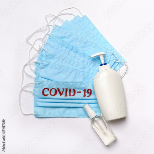 bottle of lotion, sanitizer or liquid soap and medical protective mask with COVID-19 sign over light grey background