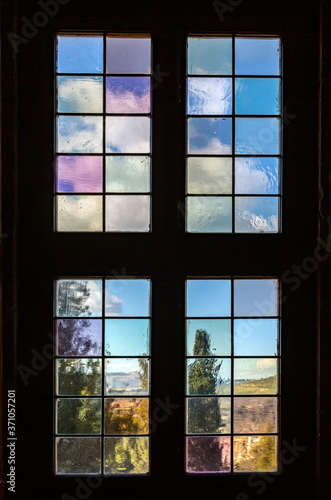 Old a window with multi-colored glass that overlooks a garden.