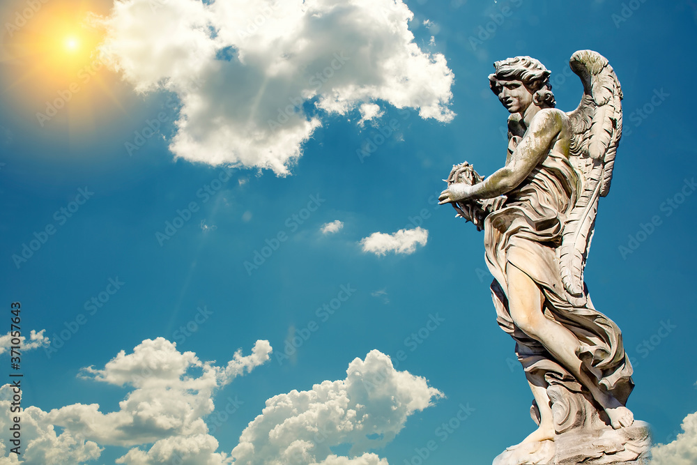 Fototapeta premium Statue of a monument to an angel on a background of blue sky and sun.