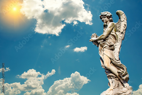 Statue of a monument to an angel on a background of blue sky and sun.
