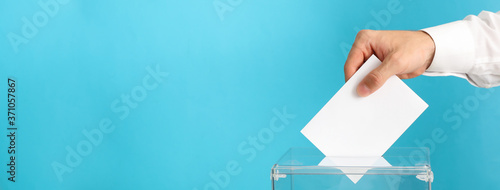 Man putting ballot into voting box on blue background photo