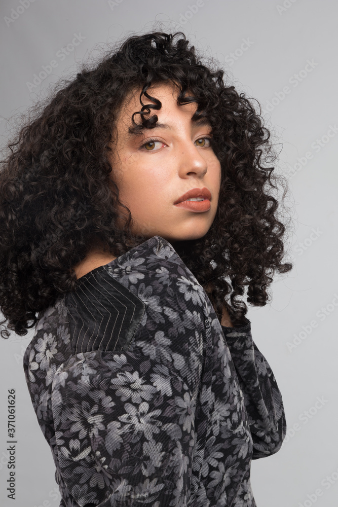 young latin woman with curly hair and brown skin from side, wearing black patterned clothing, studio with gray background young latin woman with curly hair and brown skin from side, wearing black patterned clothing, studio with gray background
