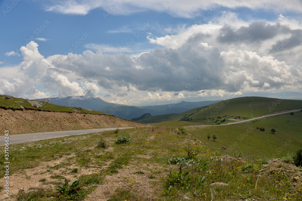 Fototapeta premium the roadbed is uneven, winding, passes through mountains and cliffs. Clouds are dark, low, with rain. A thick white fog is spreading along the road.