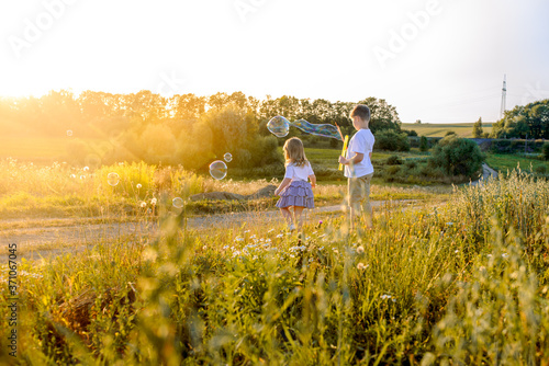 Happy children playing with soap bubbles on a summer nature. Bubbles in the sunset