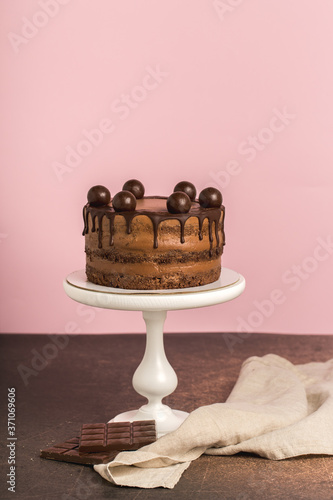 Chocolate birthday cake, white cake stand, chocolate bar, napkin,pink background.Vertical format.