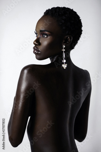 A portrait of a sexy young black female with short black hair and moist lip stick wearing a big diamond earring in front of a bright background.