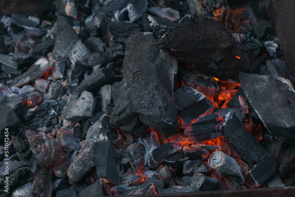 Hot coals and burning wood in the barbecue pit. Glowing and smoking charcoal, barbecue, red fire, and ash. Weekend.