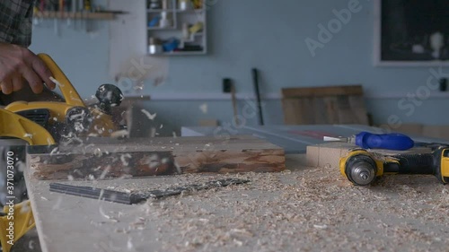 A carpenter works with an electric planer in his carpentry workshop. Slow motion footage with natural light frame.