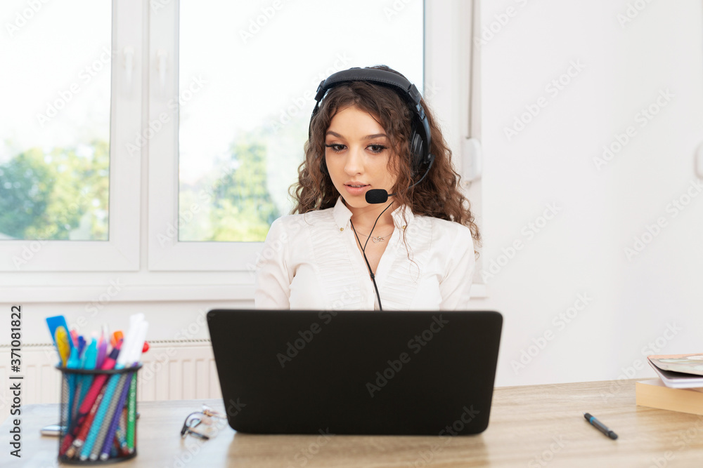 Successful brunette sitting in office by the window wearing headphones and working on laptop. Successful brunette sitting in office by the window wearing headphones and working on laptop.