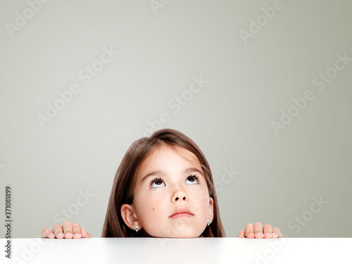 Cute little child girl looking up on the desk at school.
