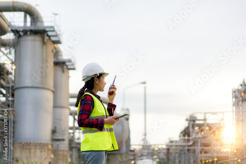 Asian woman technician Industrial engineer using walkie-talkie and holding bluprint working in oil refinery for building site survey in civil engineering project. photo