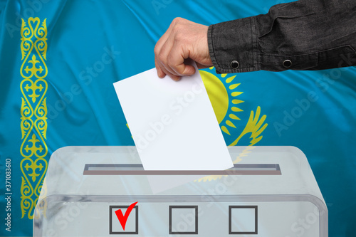male voter drops a ballot in a transparent ballot box against the background of the national flag of Kazakhstan, concept of state elections, referendum