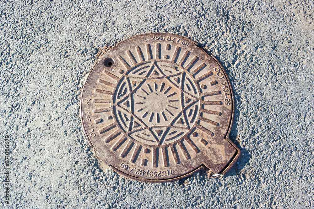 Rusty iron manhole cover with embossed sun symbol