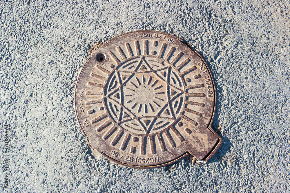 Rusty iron manhole cover with embossed sun symbol Rusty iron manhole cover with embossed sun symbol