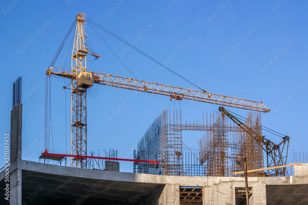 Construction site of modern apartment house with a tower crane against the clear blue sky.