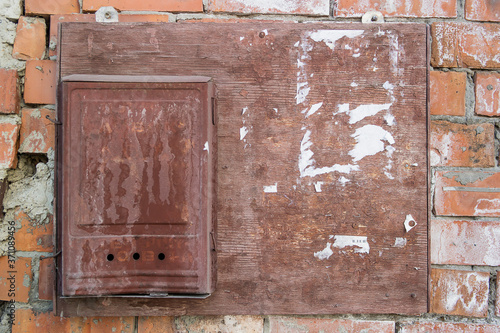 Old wooden Bulletin Board with scraps of torn paper and a bent and rusty metal mailbox hanging on a brick wall