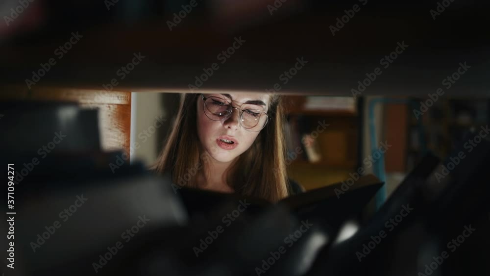 Girl glasses stands in the library and reads book with light beam coming from it. Girl glasses stands in the library and reads book with light beam coming from it.
