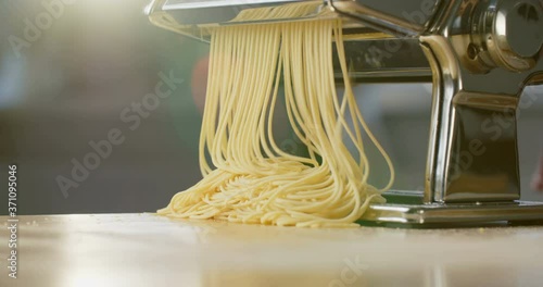 Closeup shot of a woman making fresh pasta (spaghetti) on a pasta machine at home.