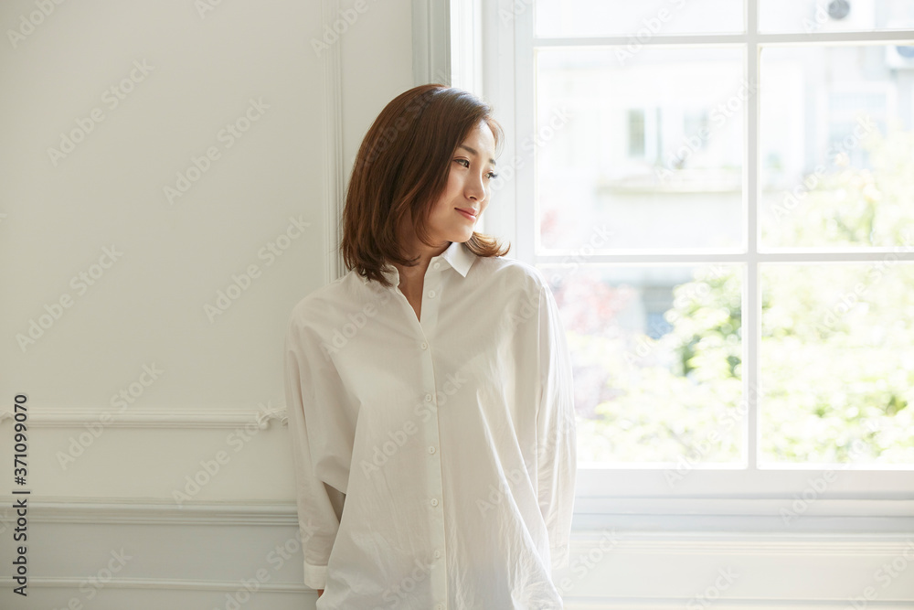 serene young asian woman staying at home standing by the window leaning against wall serene young asian woman staying at home standing by the window leaning against wall