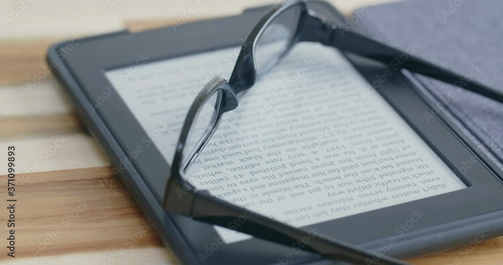 An e-reader with an open book with glasses on top of it. An e-reader with an open book with glasses on top of it.
