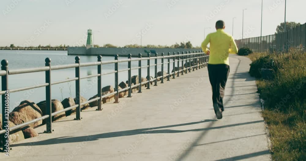 Rear view of an active senior grandfather doing sports jogging on the ocean during his morning workout. Healthy retirement and lifestyle concept. Rear view of an active senior grandfather doing sports jogging on the ocean during his morning workout. Healthy retirement and lifestyle concept.
