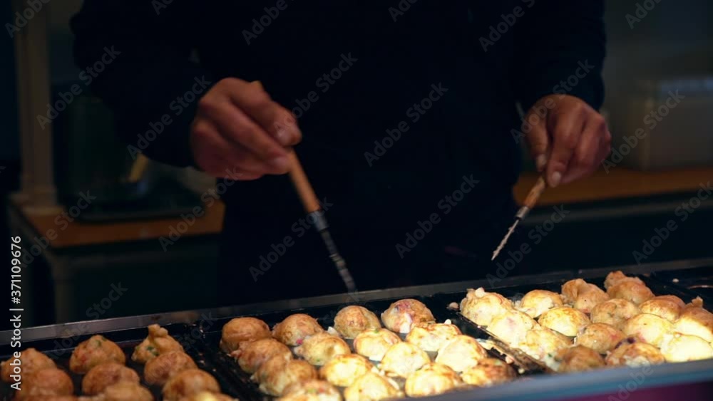 Slow motion Close up chef hands cooking Japanese snack food takoyaki in takoyaki pan at street food market in Japan. Man preparing assorted traditional Japanese meat ball eating with sweet sauce. Slow motion Close up chef hands cooking Japanese snack food takoyaki in takoyaki pan at street food market in Japan. Man preparing assorted traditional Japanese meat ball eating with sweet sauce.