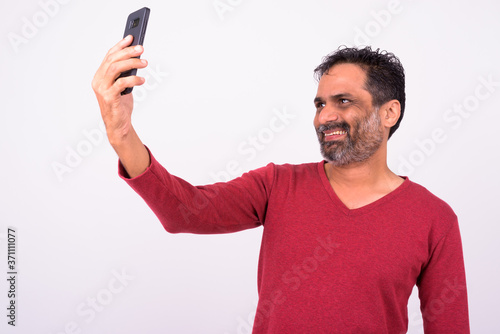 Portrait of happy mature handsome bearded Indian man taking selfie