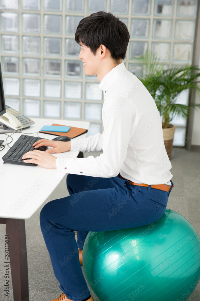 バランスボールに座って仕事をする男性 Stock Photo Adobe Stock