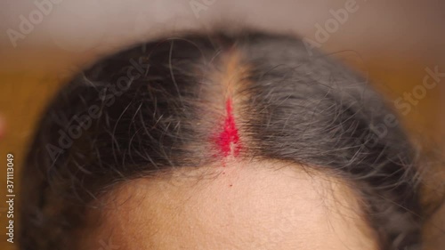 Closeup shot of Married Indian woman applying sindoor or vermilion in hair parting, photo