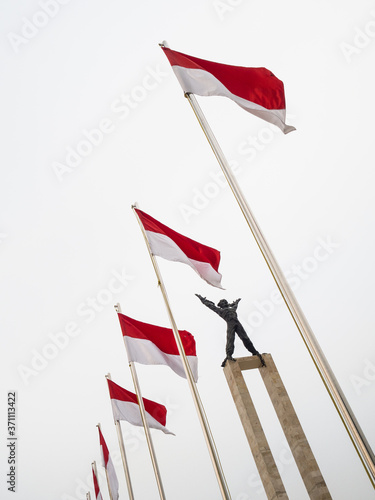 Irian Barat statue with Indonesian Flag. Lapangan Banteng, Jakarta/Indonesia - August 9 th, 2018: Monumen Pembebasan Irian Barat (English: West Irian Liberation Monument) in the morning.  photo