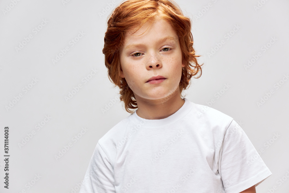 Red-haired child in a white t-shirt face close-up gray background Red-haired child in a white t-shirt face close-up gray background
