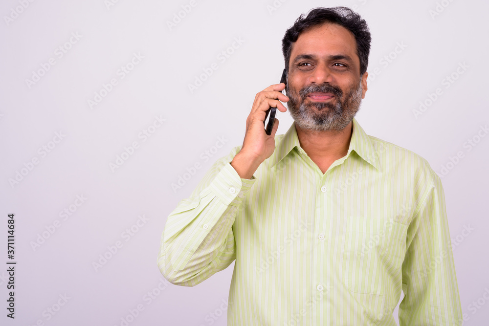 Portrait of mature handsome bearded Indian businessman talking on the phone