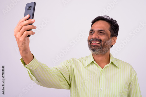 Portrait of happy mature handsome bearded Indian businessman taking selfie