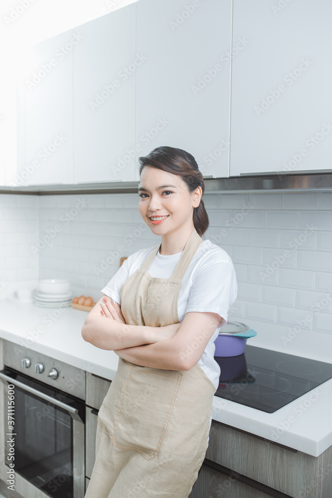 Portrait of young woman standing with arms crossed against kitchen background Portrait of young woman standing with arms crossed against kitchen background