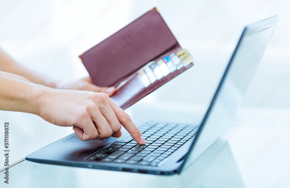Online banking, travel booking, shopping and business. Male person's hands holding an open wallet with many bank credit and debit cards while typing on a laptop computer keyboard at home. Online banking, travel booking, shopping and business. Male person's hands holding an open wallet with many bank credit and debit cards while typing on a laptop computer keyboard at home.