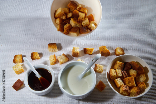 Square toasted pieces of homemade delicious rusk, hardtack, Dryasdust, zwieback, Liquid honey in a plate and cap of milk on a white tablecloth. photo