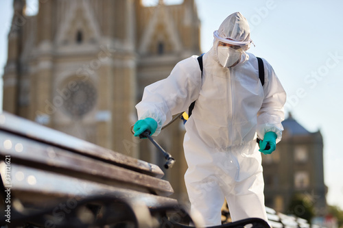 Man in hazmat suit disinfecting public bench in the city due to coronavirus epidemic.