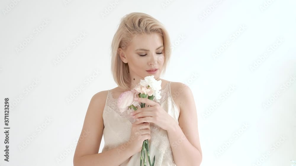 portrait of a young attractive gentle blonde woman in a white dress on a white background, who holds a bouquet of white flowers in her hands, smiles, flirts, winks portrait of a young attractive gentle blonde woman in a white dress on a white background, who holds a bouquet of white flowers in her hands, smiles, flirts, winks
