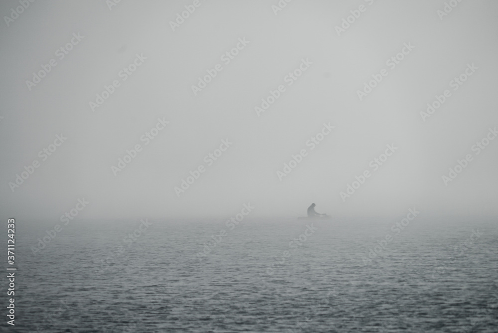 Fog over the lake. A man is sailing in a boat with an oar.