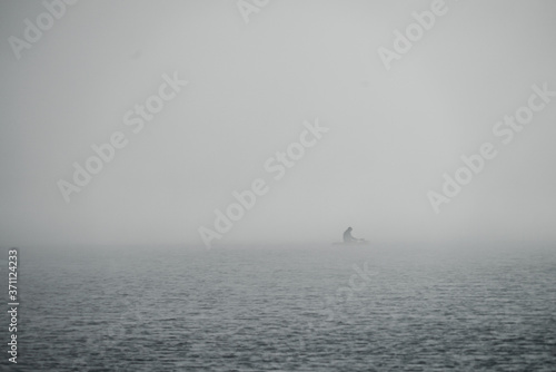 Fog over the lake. A man is sailing in a boat with an oar.