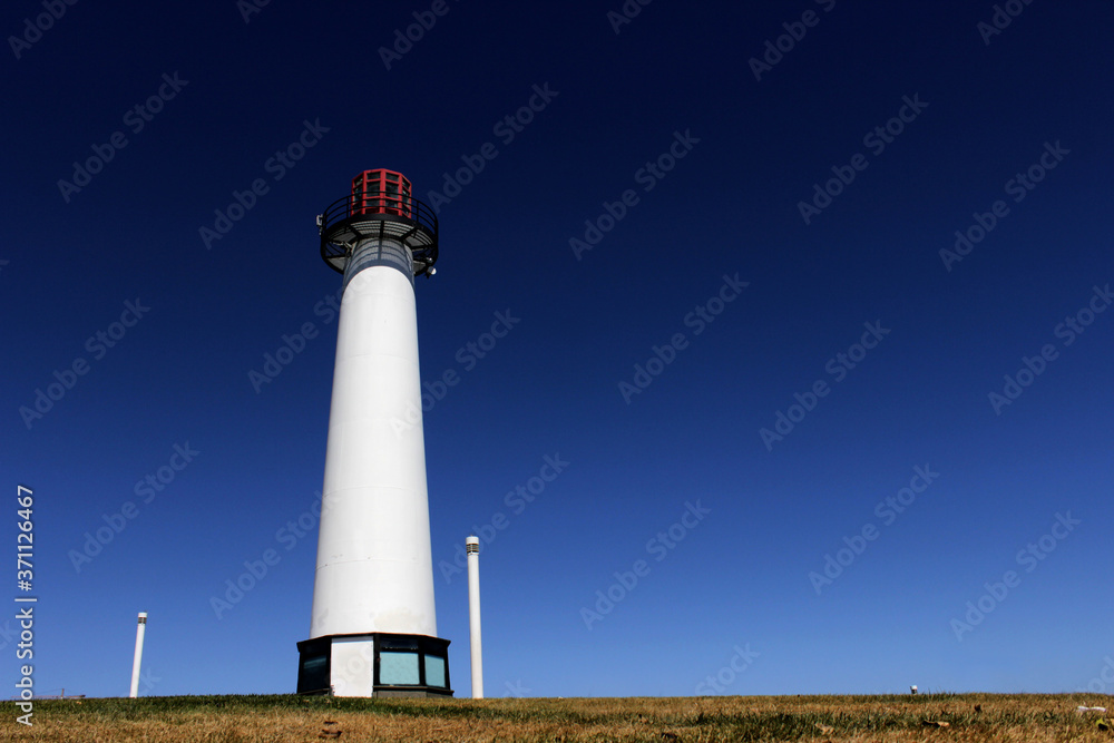A lighthouse against the blue sky on long beach near the Pacific ocean. A lighthouse near the port city.