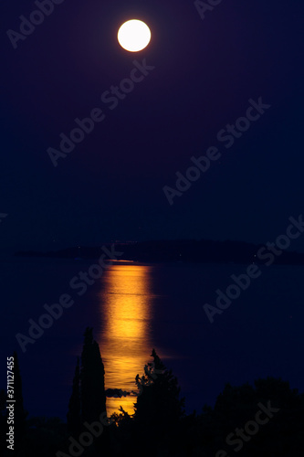 Panoramic View of Full Moon Rising Over the Sea at Corfu in Greece casting a reflection of moonlight shadow on trees and island