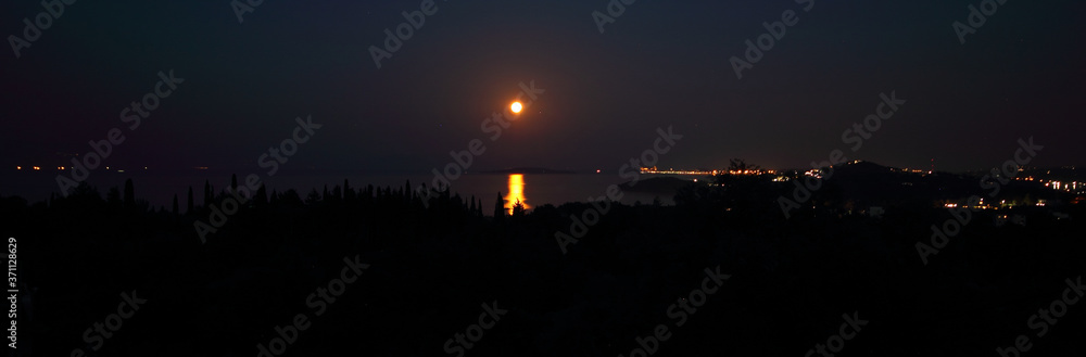 Panoramic View of Full Moon Rising Over the Sea at Corfu in Greece casting a reflection of moonlight shadow on trees and island Panoramic View of Full Moon Rising Over the Sea at Corfu in Greece casting a reflection of moonlight shadow on trees and island