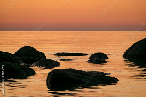 orange sunset by the sea, black stone silhouettes against the sea background, summer