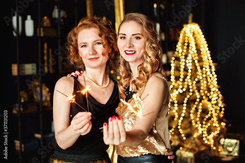 Sparklers in the hands of two beautiful girls Christmas garlands and gifts. Gold Christmas decoration. Happy New Year.